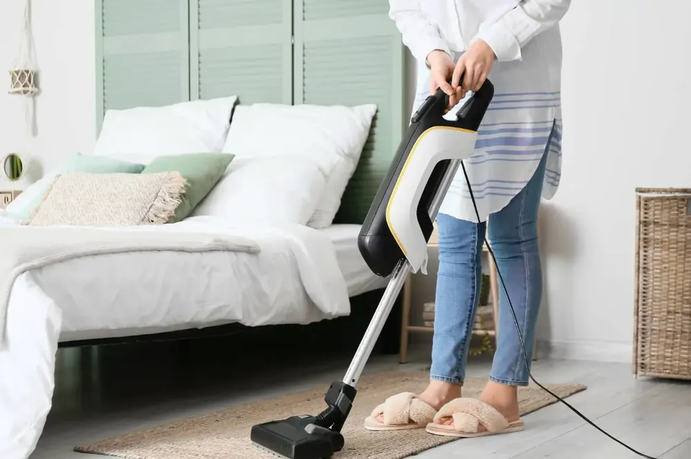 Cleaner vacuuming the floor beside a bed
